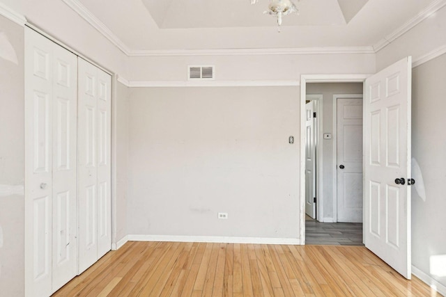 unfurnished bedroom with ornamental molding, hardwood / wood-style floors, a closet, and a tray ceiling