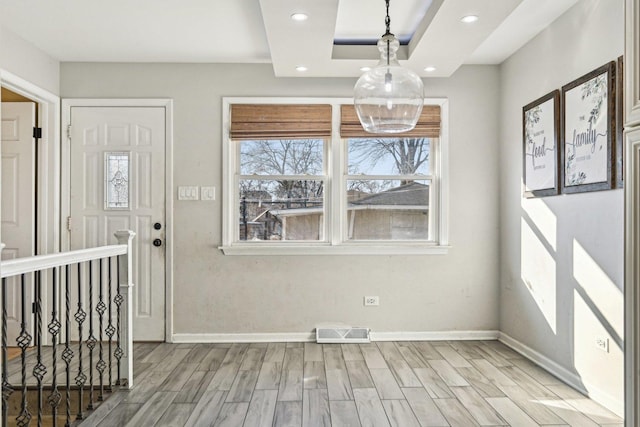 unfurnished dining area featuring a tray ceiling and light hardwood / wood-style flooring