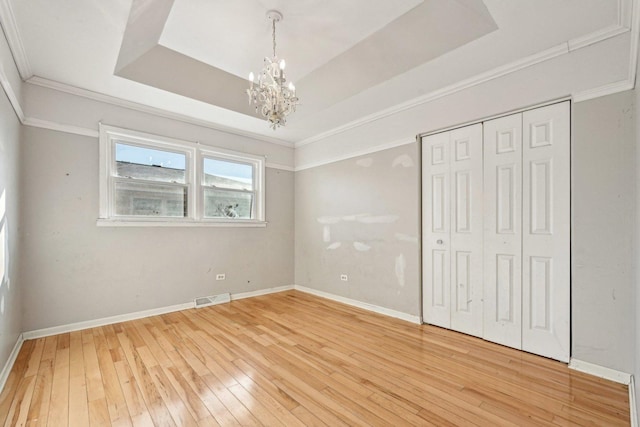 unfurnished bedroom with a chandelier, hardwood / wood-style flooring, a tray ceiling, crown molding, and a closet