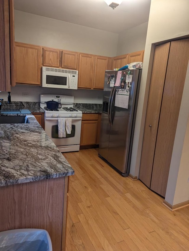 kitchen with sink, light wood-type flooring, dark stone countertops, and white appliances