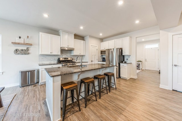 kitchen with dark stone countertops, stainless steel appliances, a kitchen breakfast bar, white cabinets, and a center island with sink