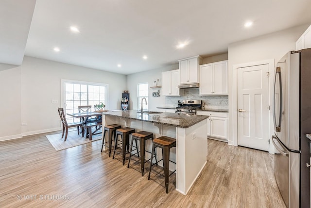 kitchen featuring stainless steel appliances, an island with sink, dark stone countertops, and white cabinets