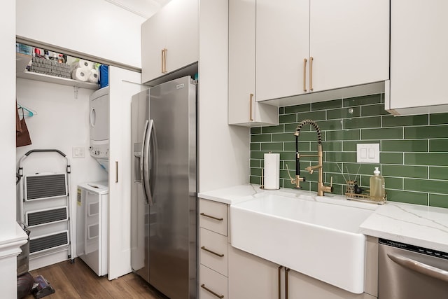 kitchen featuring white cabinetry, sink, stacked washer and dryer, stainless steel appliances, and light stone countertops