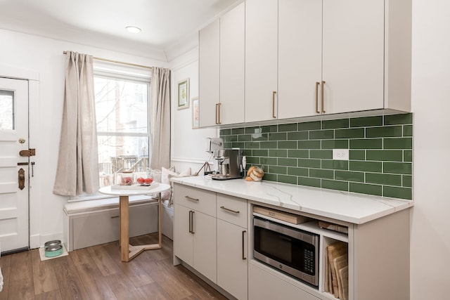 kitchen with light wood-type flooring, ornamental molding, light stone countertops, decorative backsplash, and white cabinets