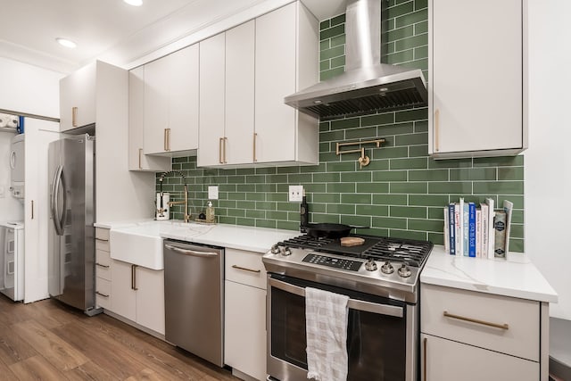 kitchen featuring stacked washer / dryer, white cabinetry, appliances with stainless steel finishes, and wall chimney range hood