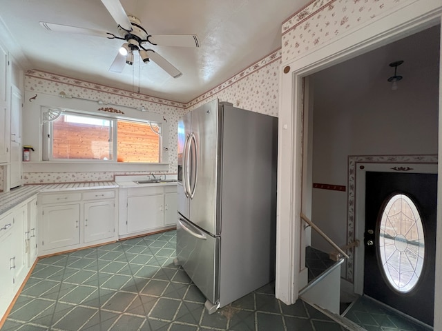 kitchen featuring stainless steel fridge with ice dispenser, ceiling fan, dark tile patterned floors, white cabinets, and sink