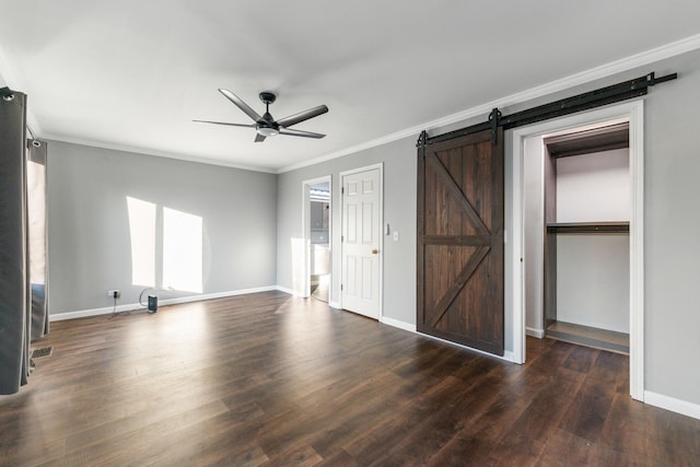 unfurnished bedroom featuring ornamental molding, a barn door, dark wood-type flooring, and ceiling fan