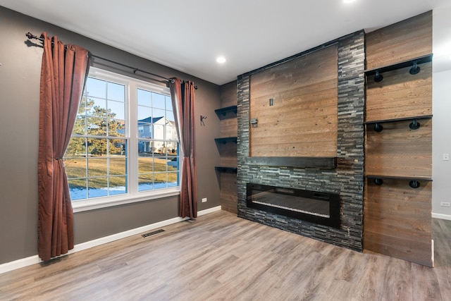 unfurnished living room featuring a healthy amount of sunlight, a stone fireplace, and light hardwood / wood-style flooring