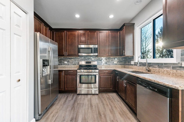 kitchen with appliances with stainless steel finishes, sink, light stone countertops, dark brown cabinets, and light wood-type flooring