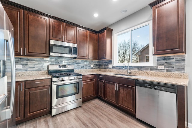 kitchen with sink, light stone counters, dark brown cabinets, light hardwood / wood-style flooring, and appliances with stainless steel finishes