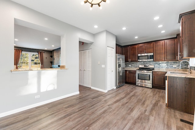 kitchen with appliances with stainless steel finishes, sink, light stone counters, dark brown cabinets, and light hardwood / wood-style flooring