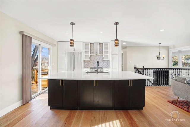 kitchen with sink, stainless steel refrigerator, tasteful backsplash, light hardwood / wood-style floors, and a large island with sink