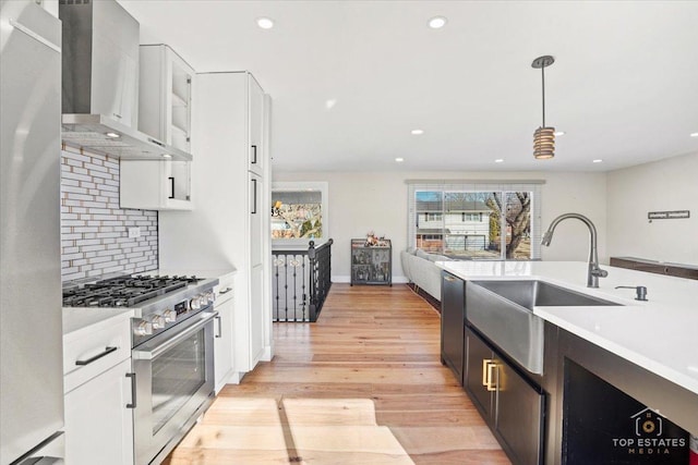 kitchen with decorative light fixtures, high end stove, white cabinets, and wall chimney exhaust hood