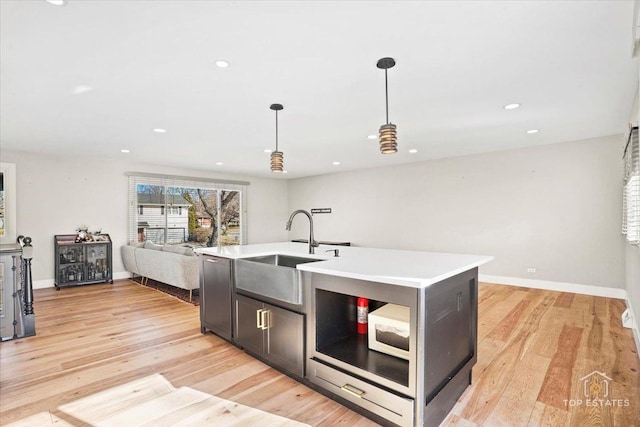 kitchen featuring pendant lighting, sink, light hardwood / wood-style floors, and an island with sink