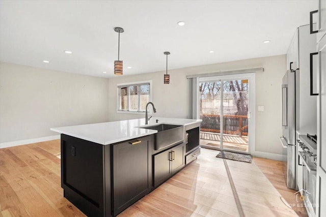 kitchen with pendant lighting, sink, a kitchen island with sink, high end fridge, and light wood-type flooring