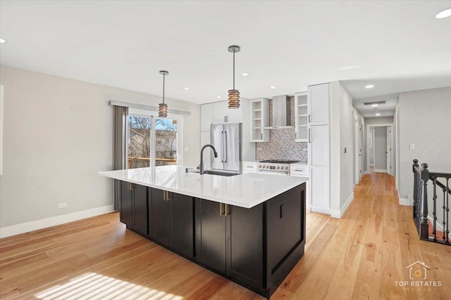 kitchen featuring white cabinetry, a kitchen island with sink, stainless steel refrigerator, and wall chimney exhaust hood