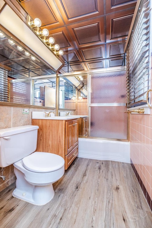 full bathroom featuring toilet, enclosed tub / shower combo, hardwood / wood-style flooring, tile walls, and vanity