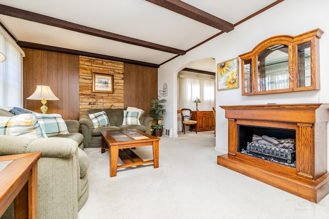 living room with a large fireplace, beam ceiling, light colored carpet, and wooden walls