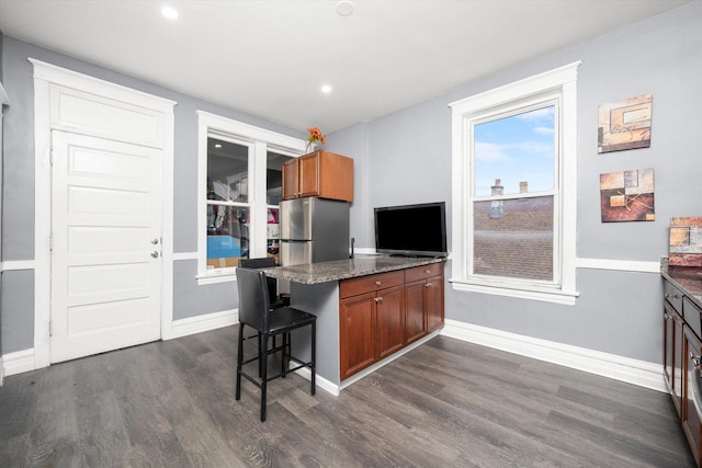 kitchen featuring a kitchen breakfast bar, dark stone countertops, dark hardwood / wood-style flooring, and stainless steel refrigerator