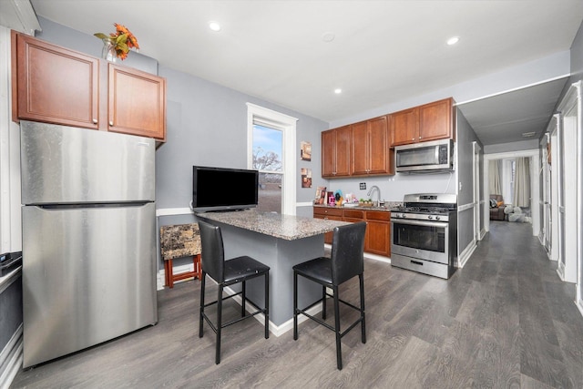 kitchen with light stone countertops, appliances with stainless steel finishes, a kitchen island, dark wood-type flooring, and a breakfast bar