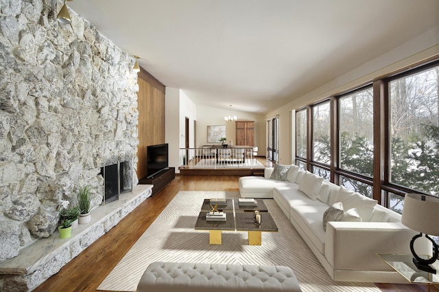 living room with an inviting chandelier, lofted ceiling, wood-type flooring, and a stone fireplace