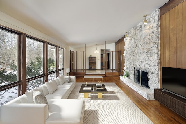 living room featuring plenty of natural light, wood-type flooring, a stone fireplace, and wooden walls