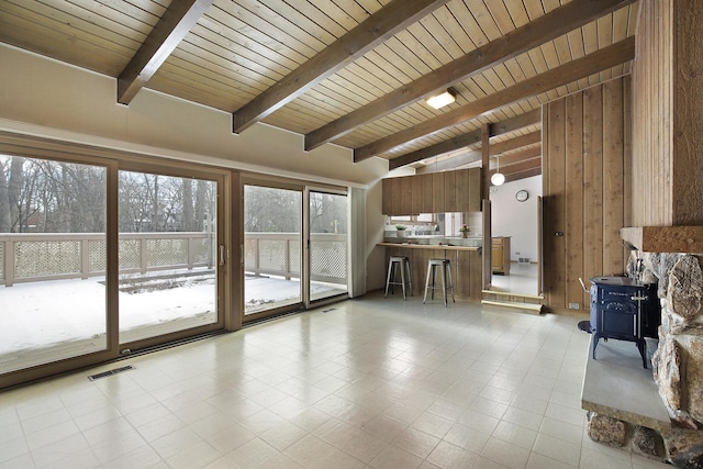 unfurnished living room featuring wooden ceiling, a wood stove, plenty of natural light, and beamed ceiling