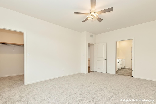 unfurnished bedroom featuring connected bathroom, a walk in closet, carpet floors, a closet, and ceiling fan