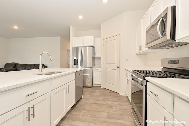 kitchen featuring appliances with stainless steel finishes, white cabinetry, sink, light stone countertops, and light hardwood / wood-style flooring