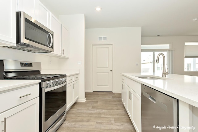 kitchen with stainless steel appliances, sink, light hardwood / wood-style flooring, and white cabinets