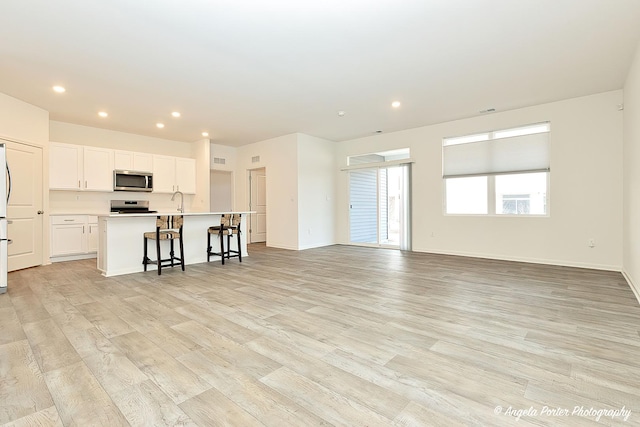 kitchen featuring appliances with stainless steel finishes, a breakfast bar, white cabinets, a center island with sink, and light hardwood / wood-style flooring