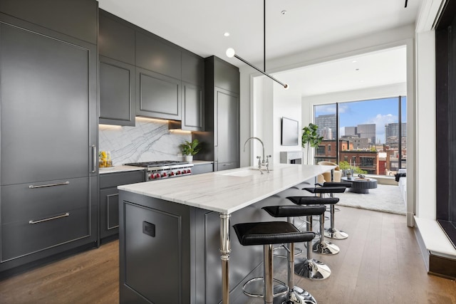 kitchen with a center island with sink, a breakfast bar, sink, tasteful backsplash, and light stone counters