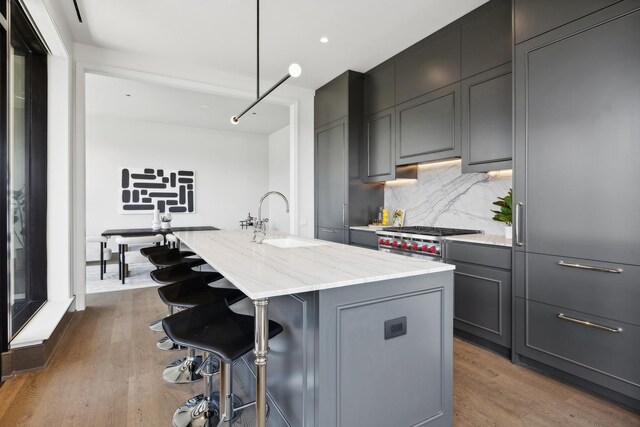 kitchen featuring pendant lighting, an island with sink, sink, high end stove, and light stone counters