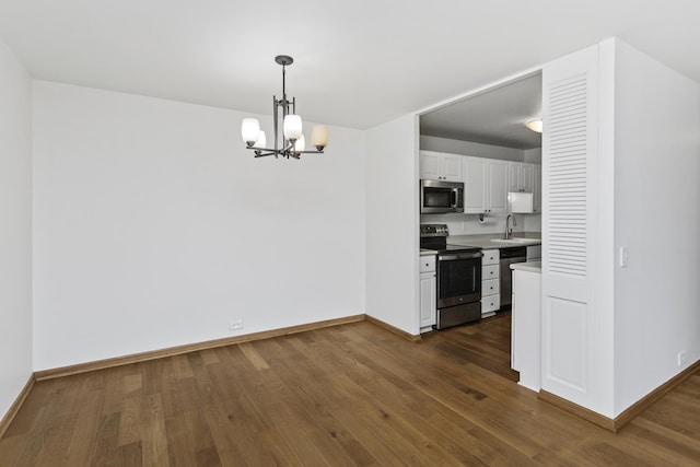 kitchen with appliances with stainless steel finishes, white cabinetry, sink, hanging light fixtures, and dark wood-type flooring