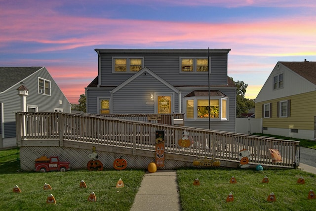 back house at dusk with a deck and a lawn