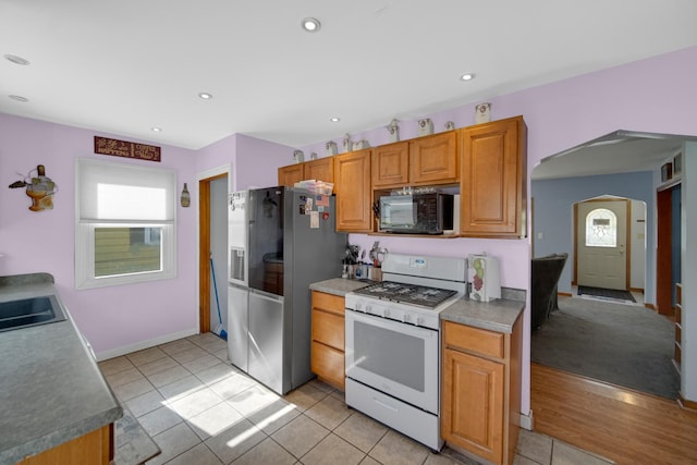 kitchen with light tile patterned floors, stainless steel refrigerator with ice dispenser, sink, and white range with gas cooktop