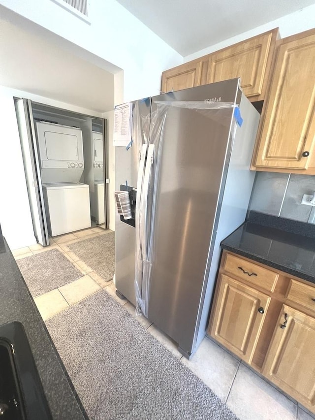 kitchen featuring light tile patterned floors, tasteful backsplash, stacked washer and dryer, and stainless steel refrigerator