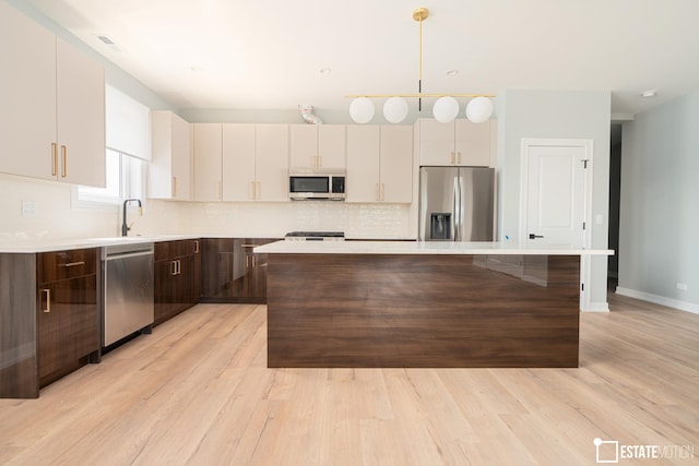 kitchen with tasteful backsplash, pendant lighting, a kitchen island, light hardwood / wood-style flooring, and appliances with stainless steel finishes