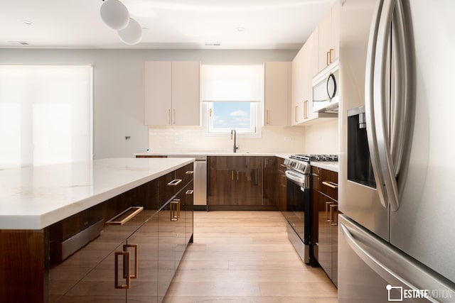 kitchen with appliances with stainless steel finishes, dark brown cabinetry, white cabinetry, sink, and light hardwood / wood-style flooring