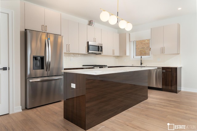 kitchen with pendant lighting, appliances with stainless steel finishes, a center island, light hardwood / wood-style floors, and sink