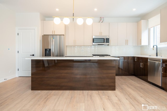 kitchen with stainless steel appliances, decorative backsplash, dark brown cabinets, a kitchen island, and light hardwood / wood-style flooring