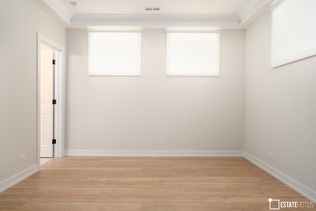 empty room with a tray ceiling, ornamental molding, and light hardwood / wood-style flooring