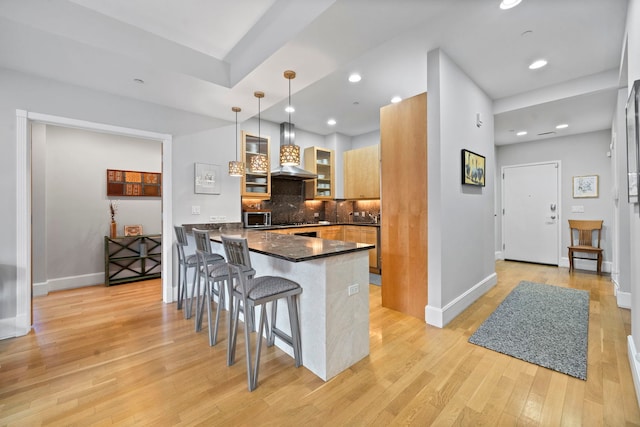 kitchen with pendant lighting, a breakfast bar area, backsplash, wall chimney exhaust hood, and light hardwood / wood-style flooring