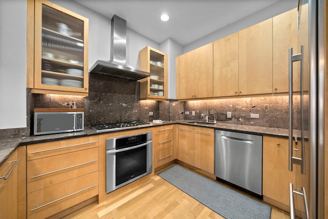 kitchen with appliances with stainless steel finishes, sink, dark stone counters, and wall chimney exhaust hood