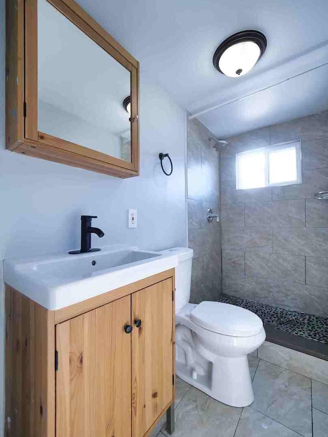 bathroom featuring toilet, vanity, tile patterned flooring, and a tile shower