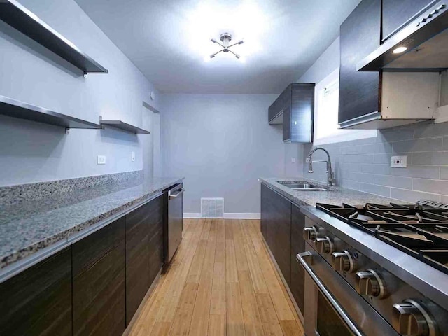 kitchen with appliances with stainless steel finishes, tasteful backsplash, light wood-type flooring, light stone countertops, and sink