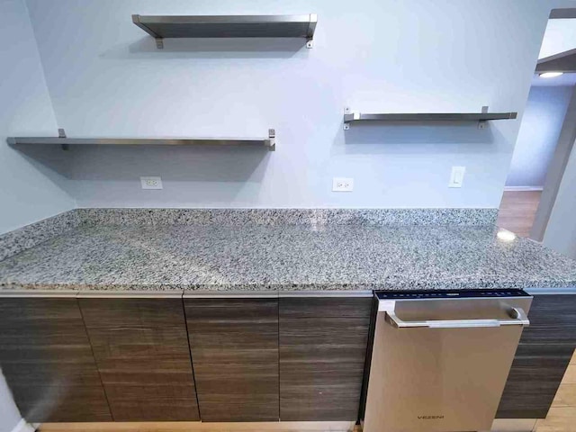 kitchen with light stone counters, dishwasher, and dark brown cabinets