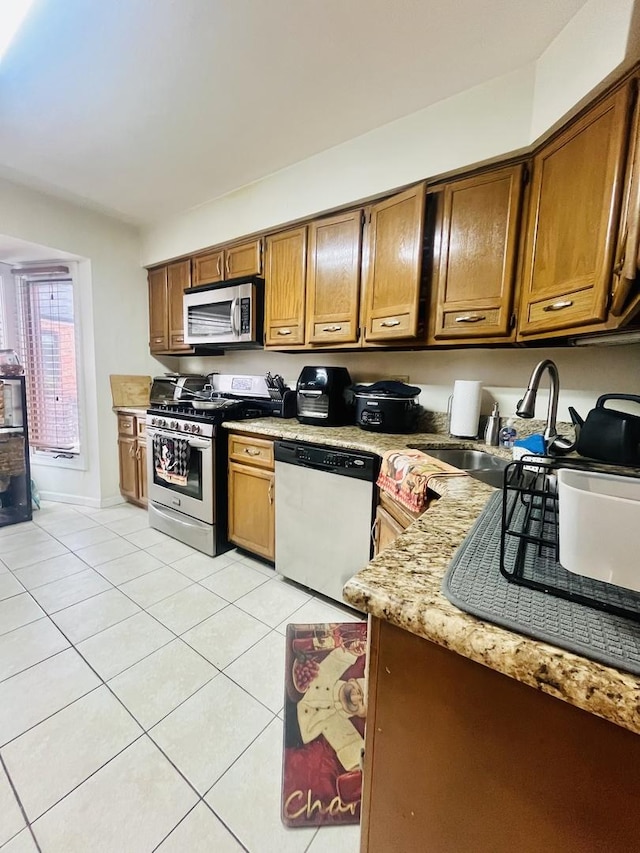 kitchen featuring light stone countertops, sink, light tile patterned floors, and stainless steel appliances