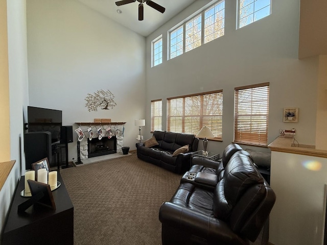 living area featuring a towering ceiling, carpet, a fireplace, and a ceiling fan