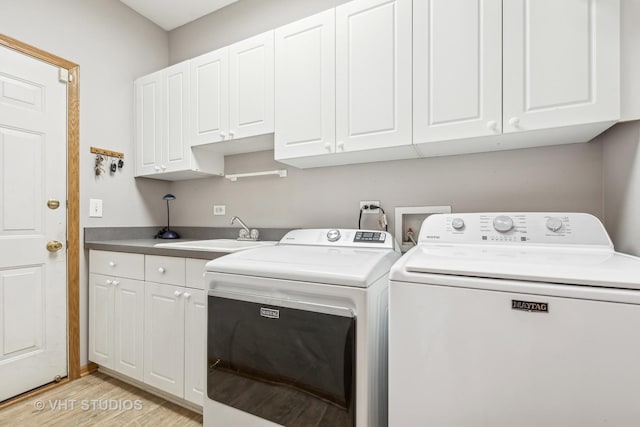 laundry room featuring cabinet space, washer and dryer, light wood finished floors, and a sink